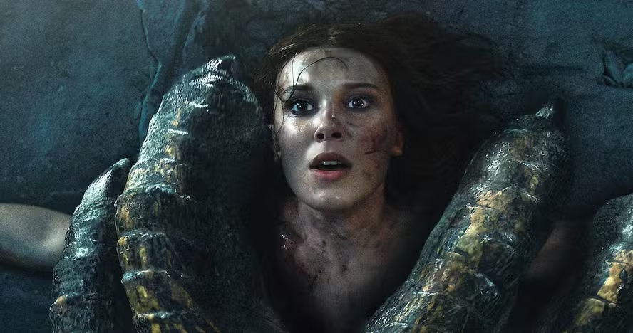 Elodie, ferida e suja, presa ao chão pelas garras de um dragão