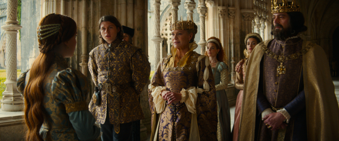 Elodie está de costas para o príncipe, a rainha e o rei, todos em trajes de realeza