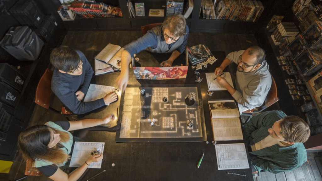 Jogadores de RPG envolta de uma mesa de madeira. 