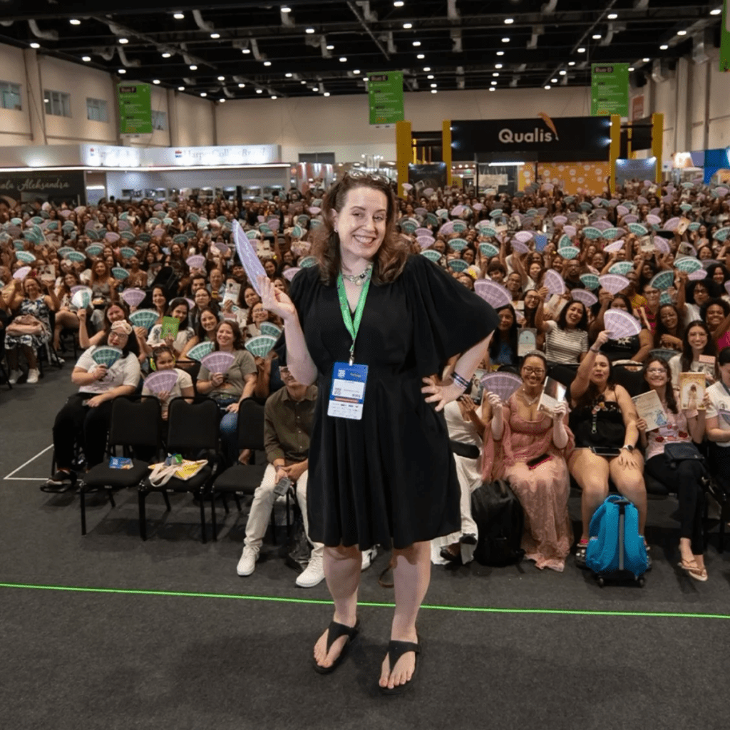 A autora Julia Quinn em frente a uma plateia segurando leques.